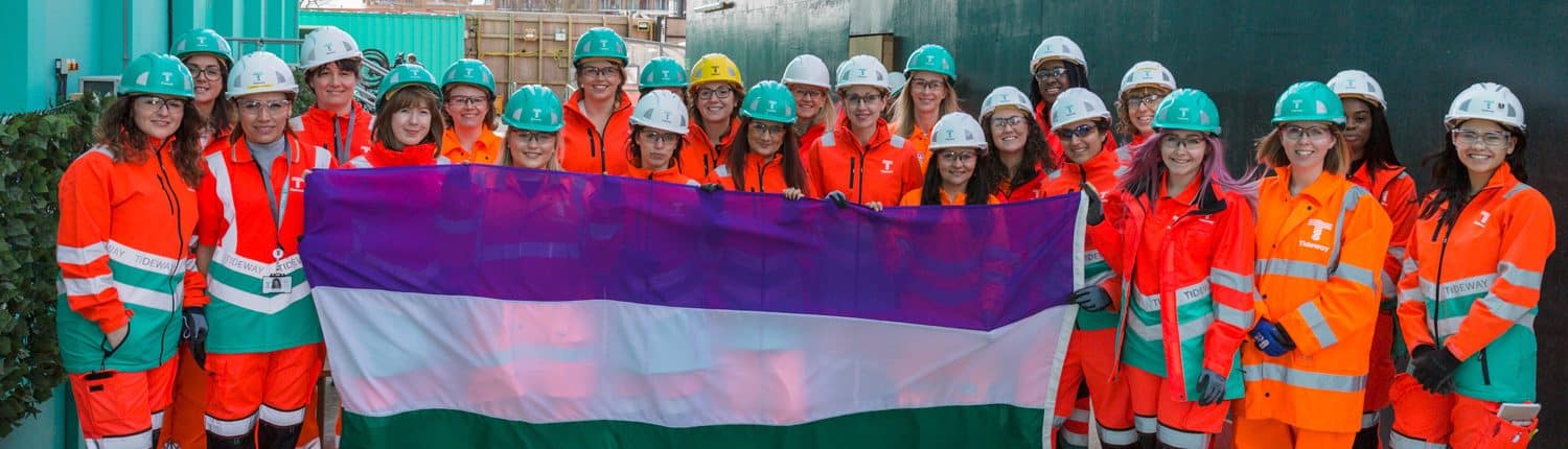 Women Crossrail workers on site holding suffragette flag